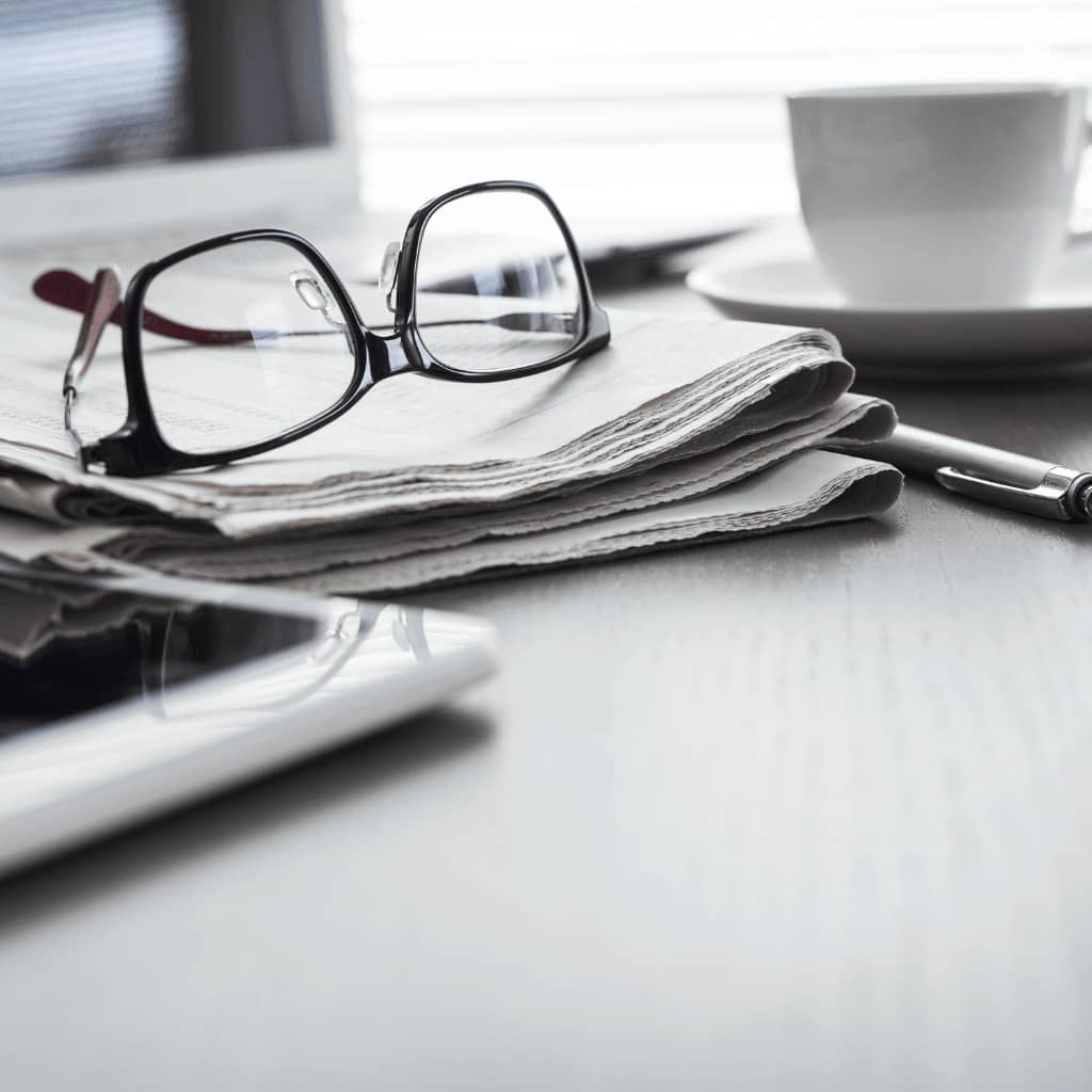 Brille liegt auf einer zusammengefalteten Zeitung, daneben steht eine weiße Tasse